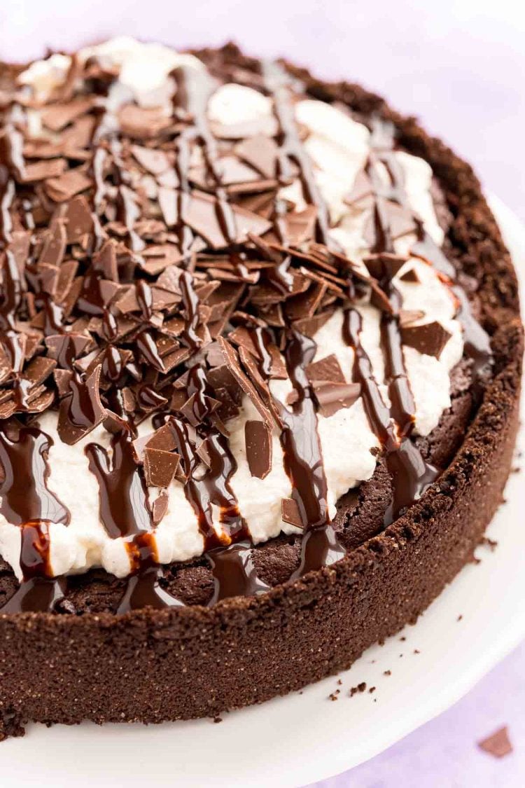 Close up photo of a Mississippi Mud Pie on a white cake stand with chocolate pieces and chocolate drizzle on top.