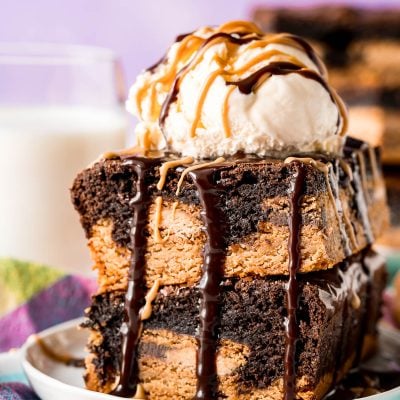 Two slutty brownies stacked on top of each other and topped with a scoop of vanilla ice cream and drizzled with peanut butter and hot fudge sauce.