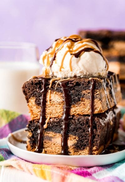 Two slutty brownies stacked on top of each other and topped with a scoop of vanilla ice cream and drizzled with peanut butter and hot fudge sauce.