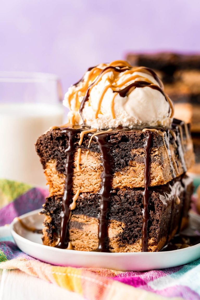 Two slutty brownies stacked on top of each other and topped with a scoop of vanilla ice cream and drizzled with peanut butter and hot fudge sauce.