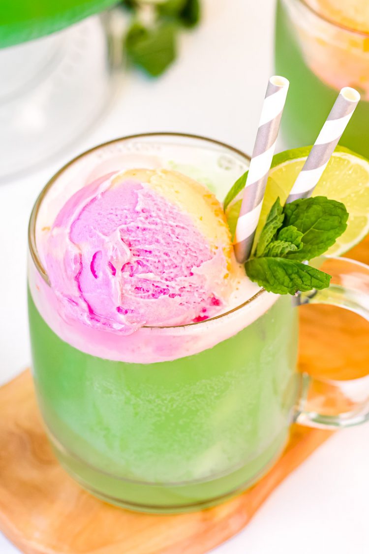 Close up photo of a mug filling with green punch topped with rainbow sherbet and garnished with lime slice and mint.