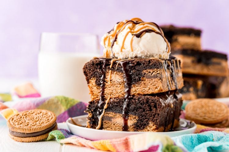 Close up photo of brownies stacked on a white plate with more brownies in the background with a glass of milk.