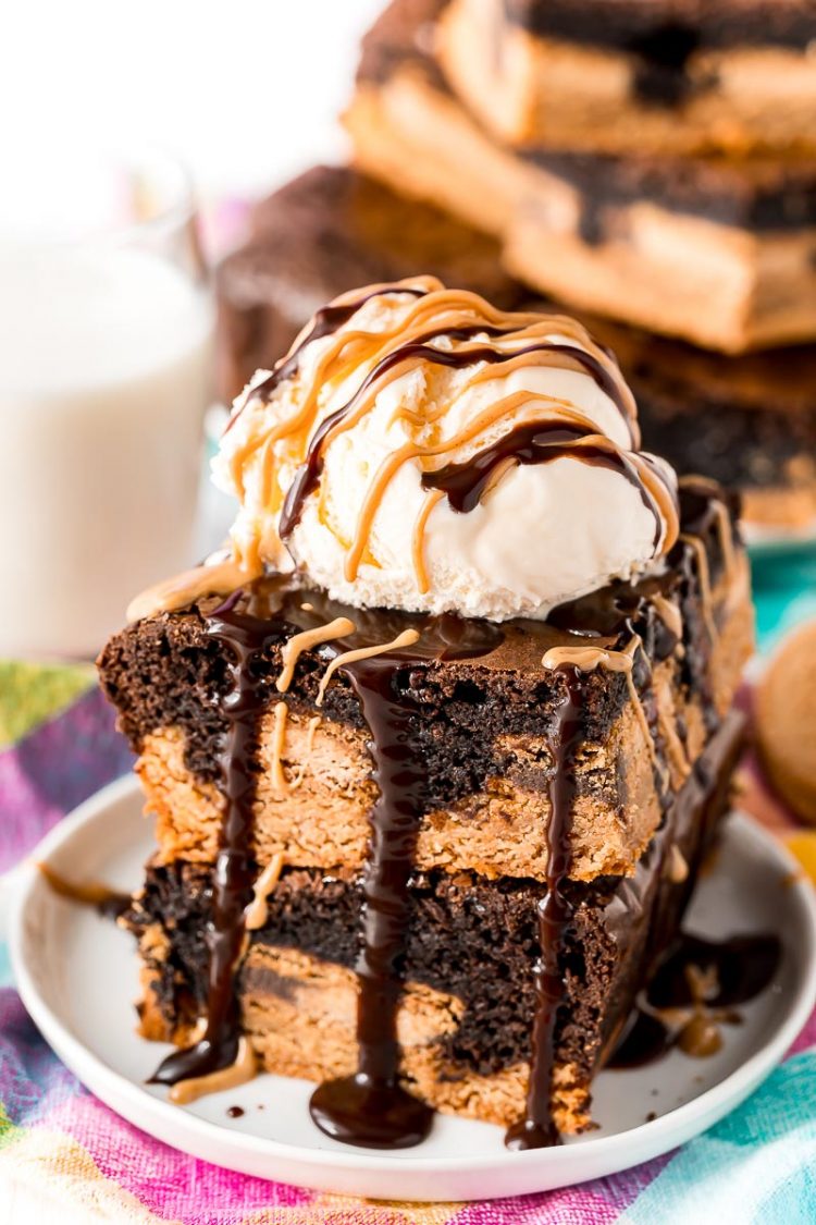 Close up photo of slutty brownies stacked on top of eachother and topped with ice cream and peanut butter and hot fudge sauce.