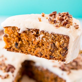 A slice of carrot cake on a server being lifted off a cake stand.