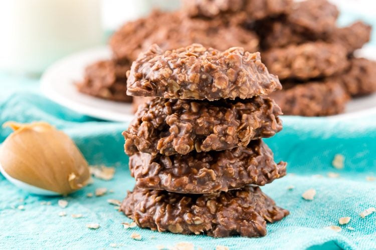 Landscape photo of a stack of no bake cookies on a blue napkin with a plate of cookies in the background.