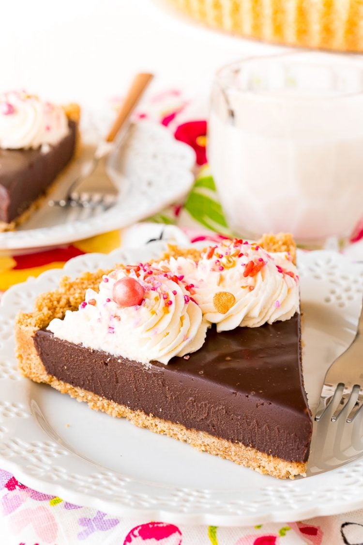 Slice of chocolate tart topped with whipped cream and sprinkles sitting on a white plate.