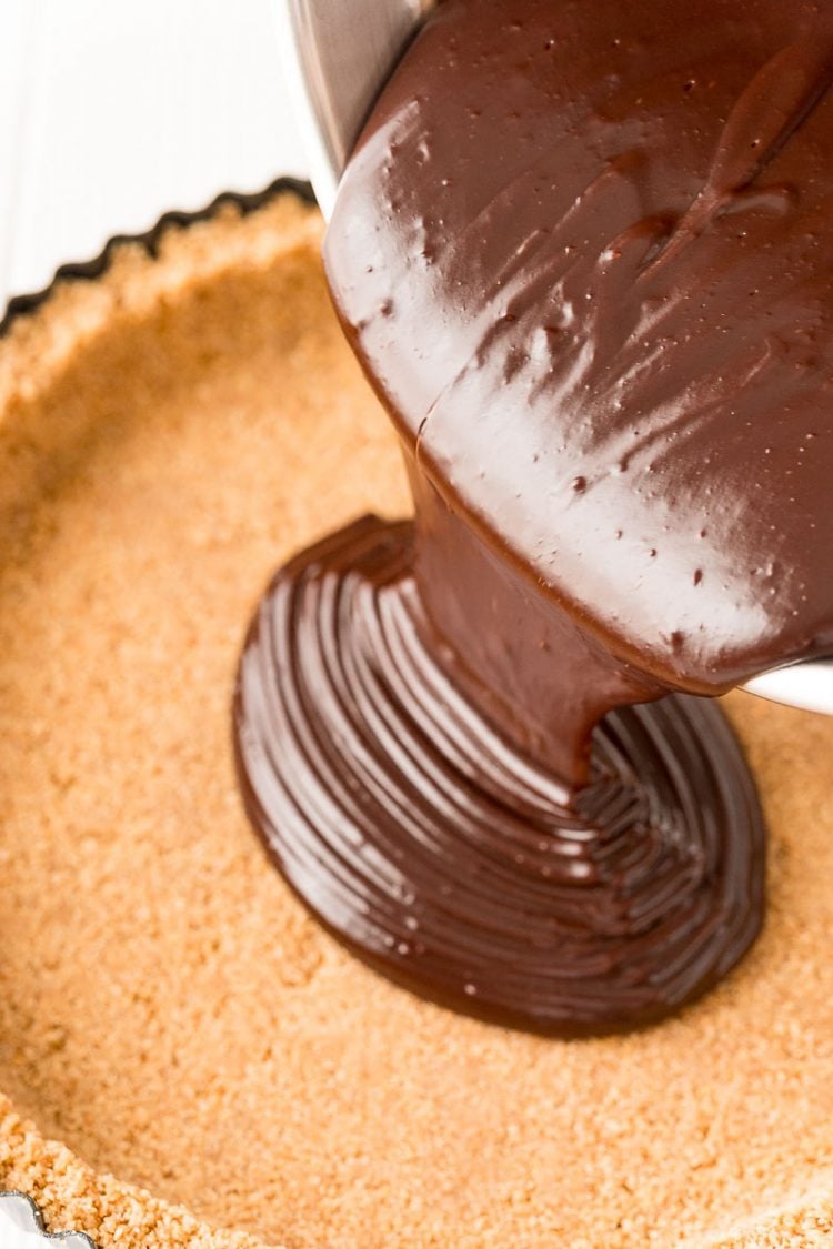 Chocolate ganache being poured into a graham cracker crust.