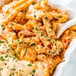 Baked ziti in a white casserole dish with a white serving spoon.