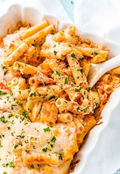 Baked ziti in a white casserole dish with a white serving spoon.