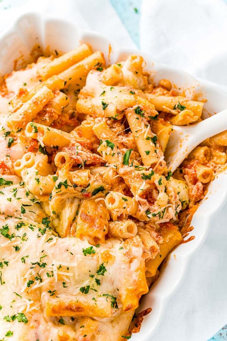 Baked ziti in a white casserole dish with a white serving spoon.