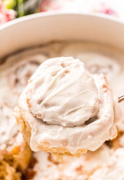 A cinnamon roll covered in icing being taken out of the pan.