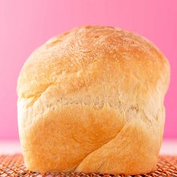 A loaf of white bread sitting on a cooling rack on to colorful napkin.