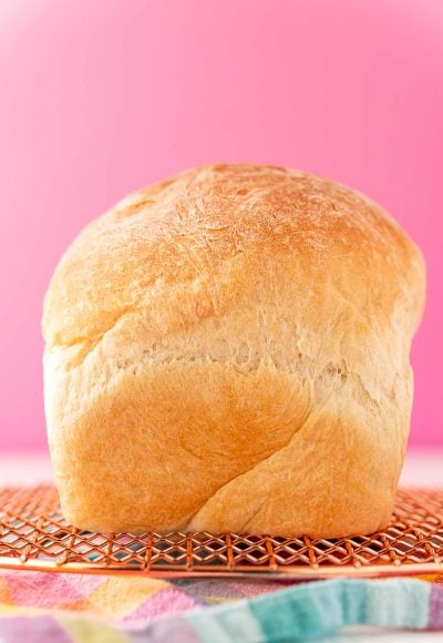 A loaf of white bread sitting on a cooling rack on to colorful napkin.