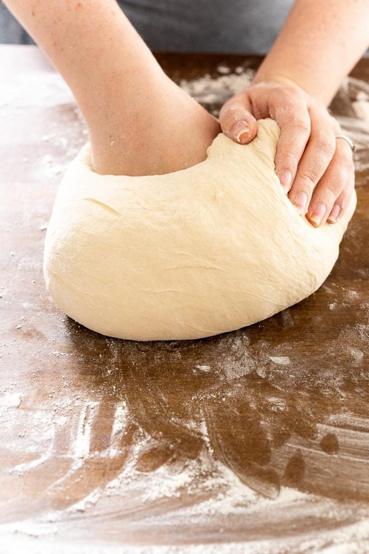 Woman kneading bread dough on a butcher block counter top.