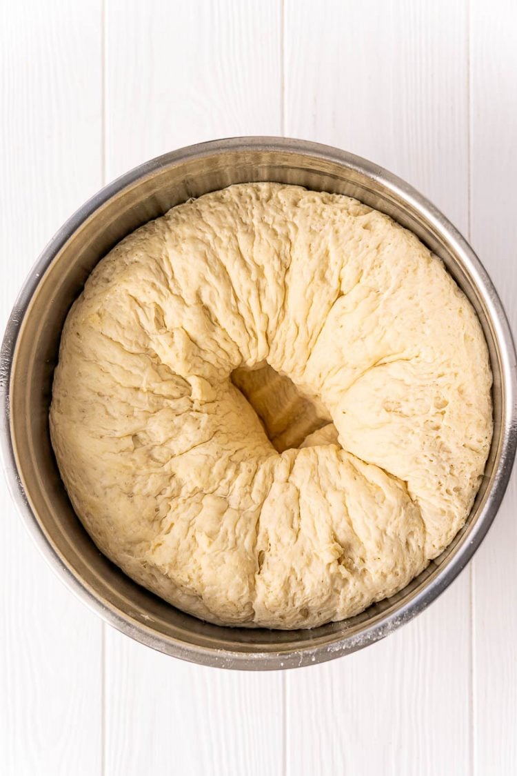 Bread dough in a metal bowl that has been punched down in the center after rising.