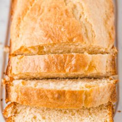 Loaf of bread on a white cutting board partially sliced.