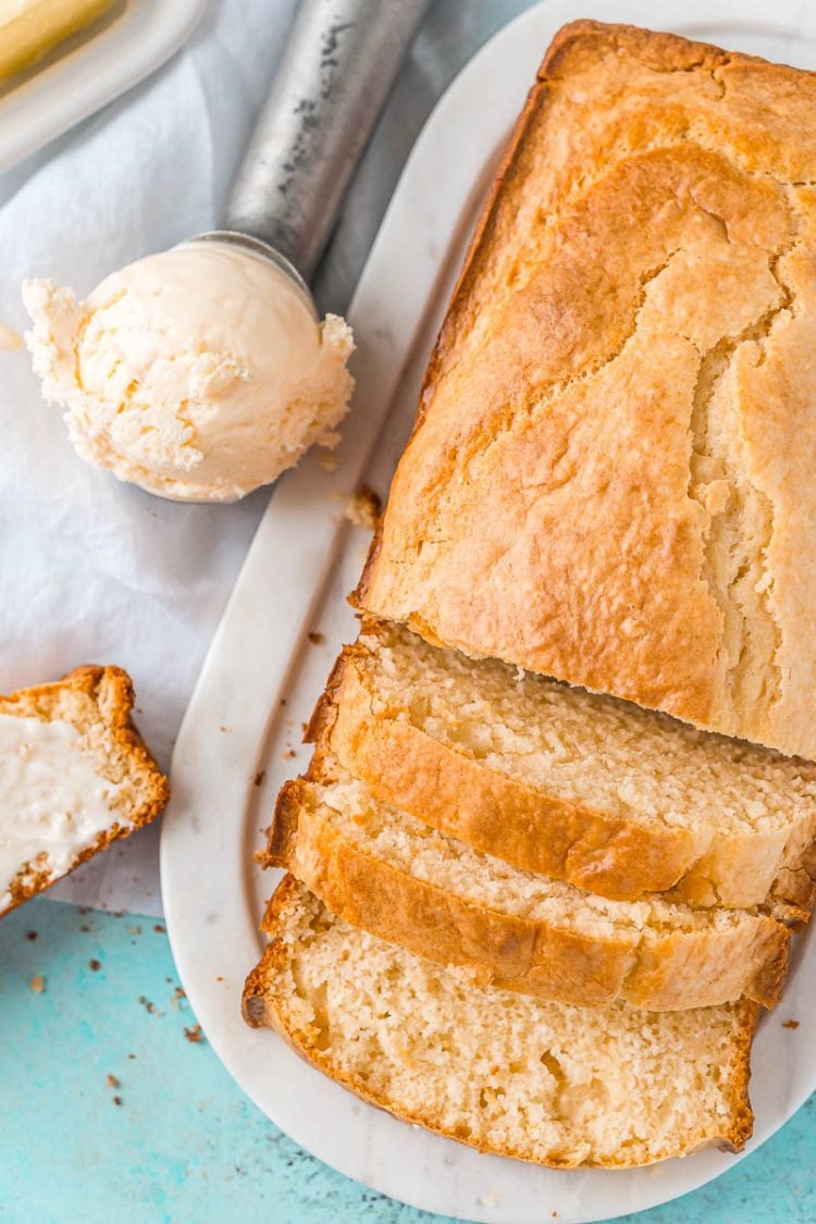 Overhead photo of a loaf of ice cream bread with a ice cream scoop with ice cream sitting next to it. Bread has been slice half way.