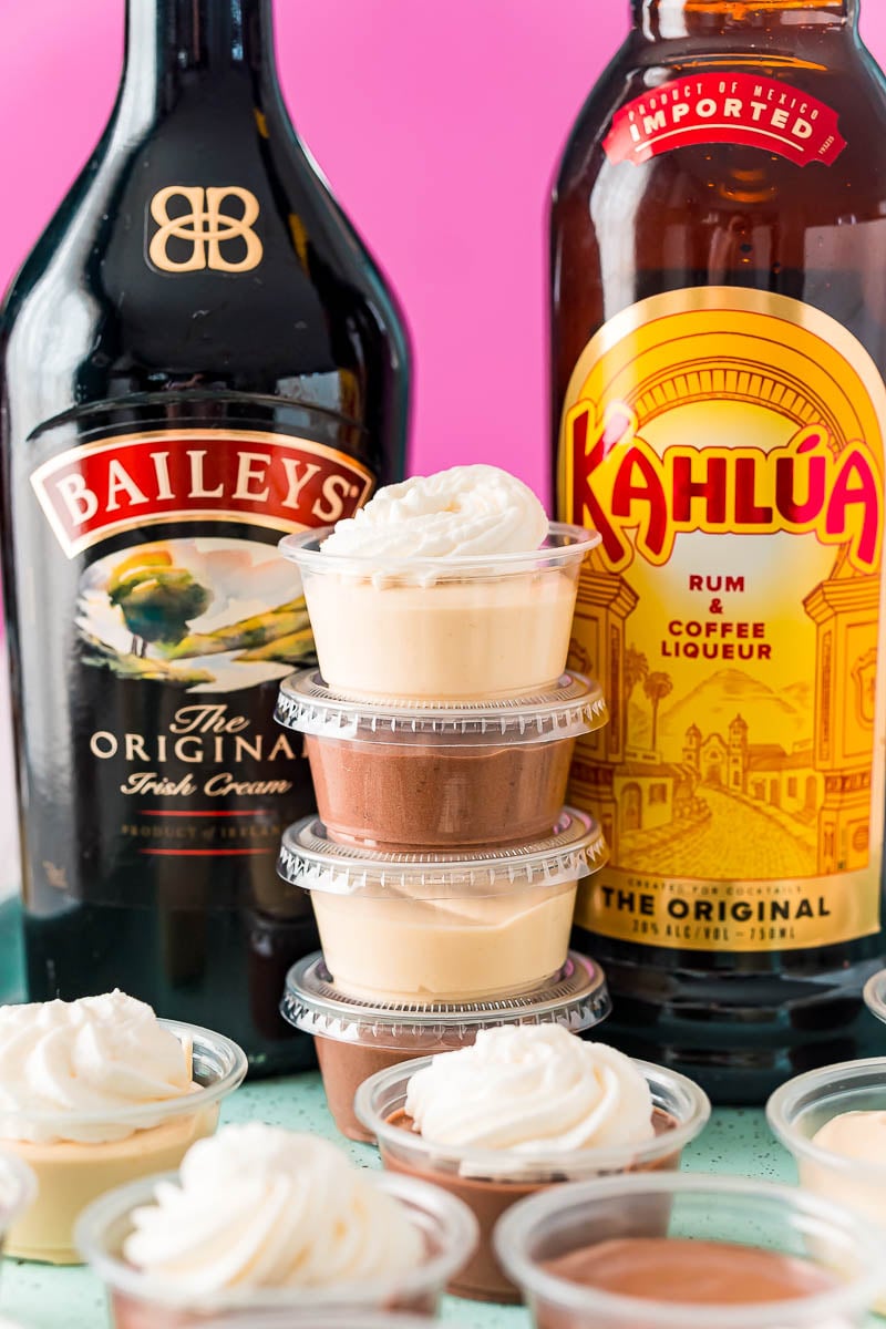 Stack of pudding shots between a bottle of Baileys and a bottle of Kahlua.