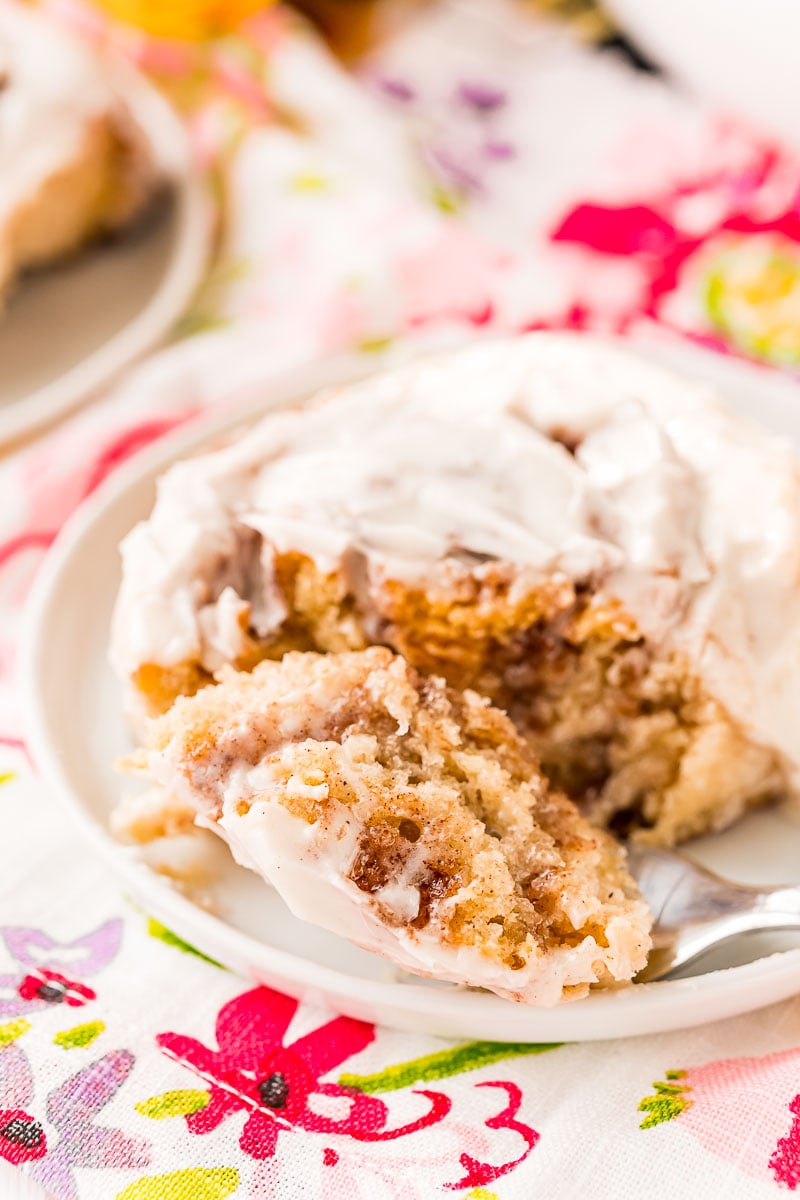 Cinnamon roll on a white plate with a bite on a fork.