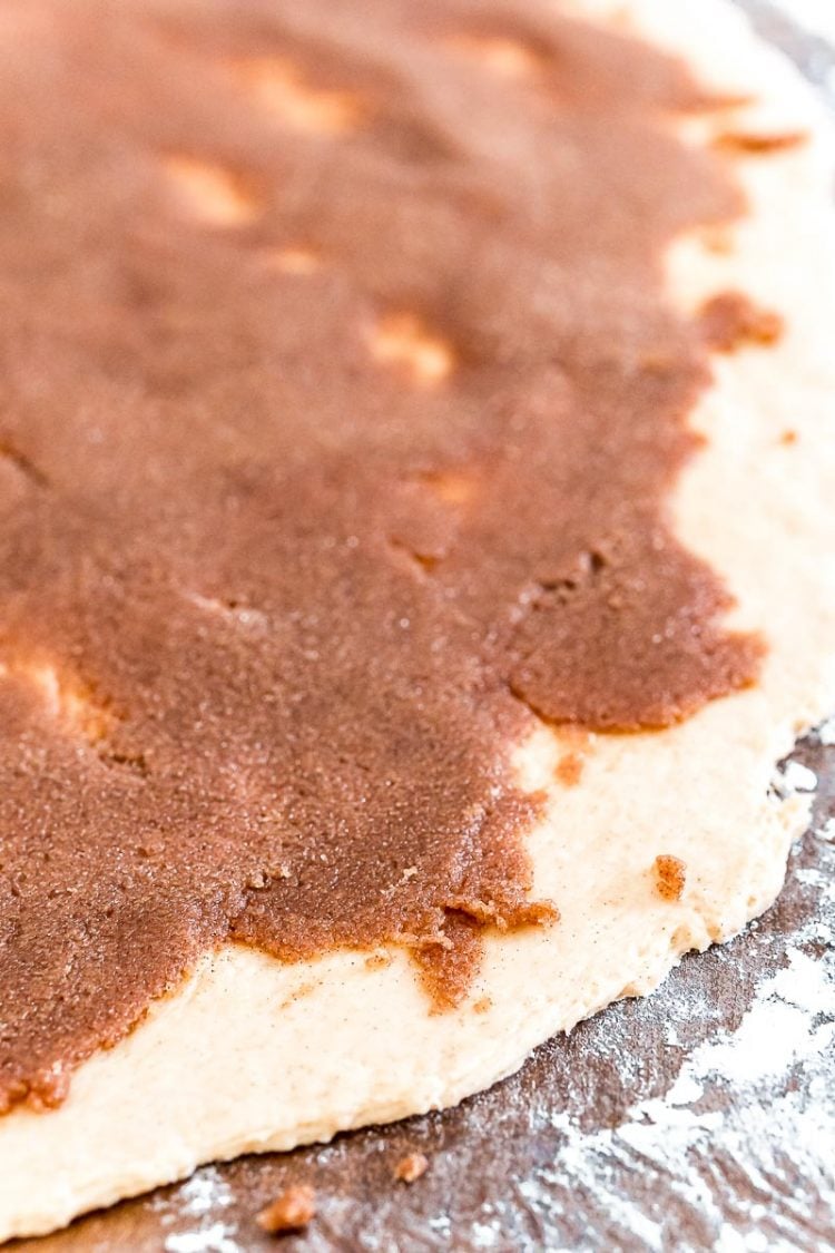 Cinnamon roll filling spread on dough on a floured surface.