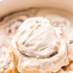 A cinnamon roll covered in icing being taken out of the pan.