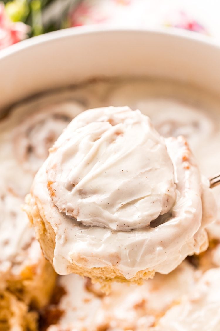 A cinnamon roll covered in icing being taken out of the pan.