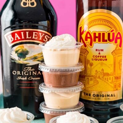 Stack of pudding shots between a bottle of Baileys and a bottle of Kahlua.