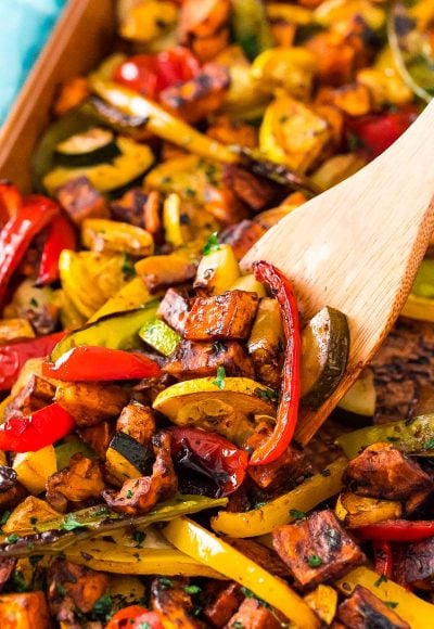 A wooden spatula scooping roasted vegetables off of a sheet pan.