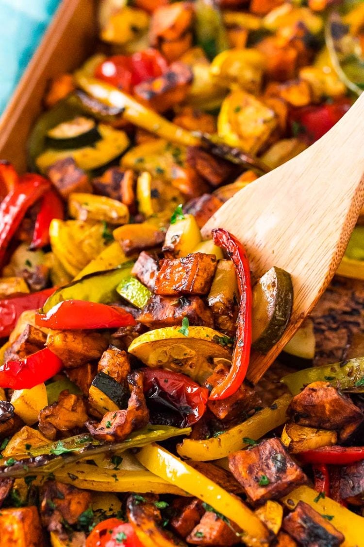 A wooden spatula scooping roasted vegetables off of a sheet pan.