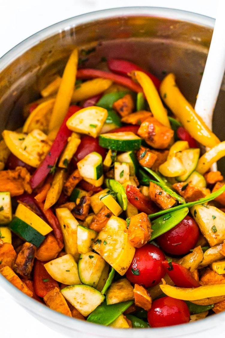 Vegetables being tossed in a bowl with dressing before roasting.