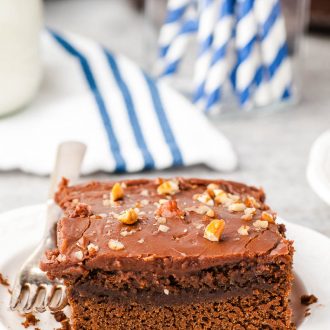 Slice of Chocolate Buttermilk Cake on a white plate with a blue and white napkin in the background.