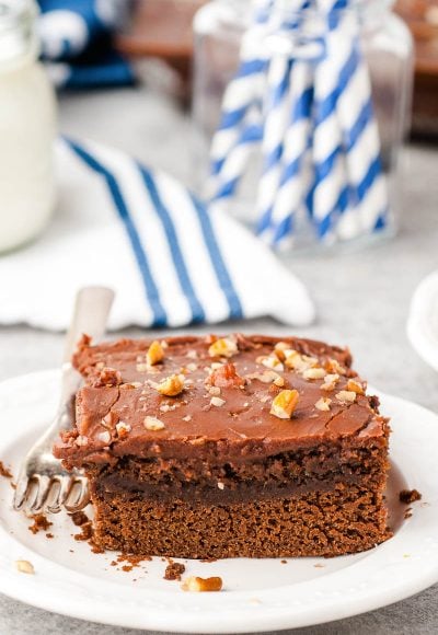 Slice of Chocolate Buttermilk Cake on a white plate with a blue and white napkin in the background.