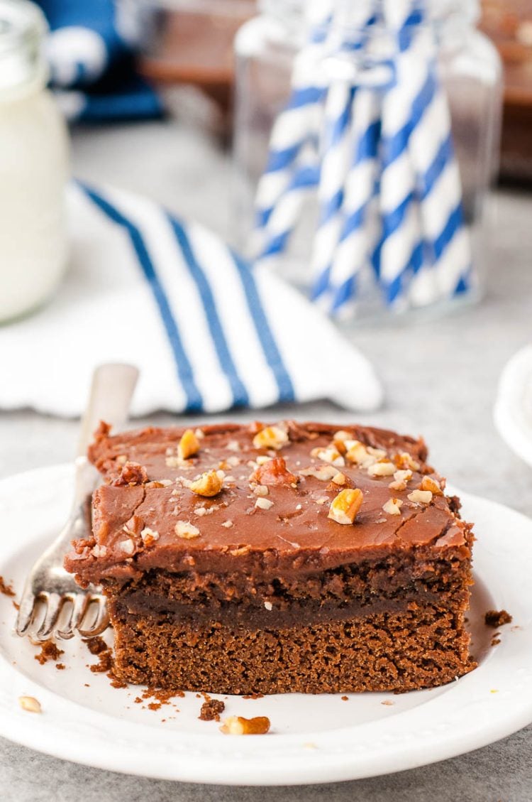 Slice of Chocolate Buttermilk Cake on a white plate with a blue and white napkin in the background.