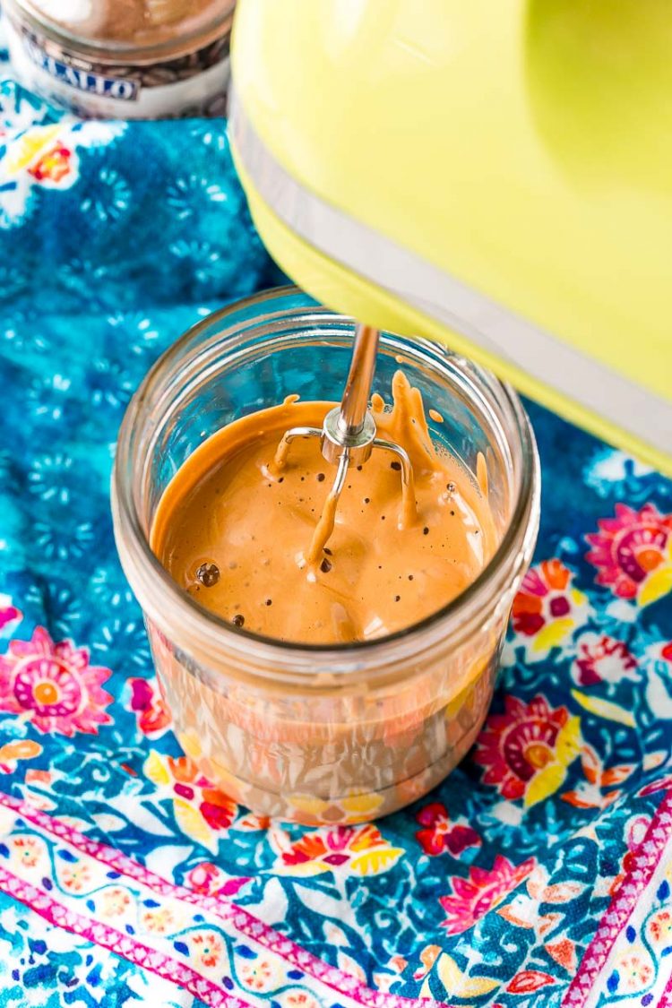 Hand mixer with one beater making whipped coffee in a mason jar.