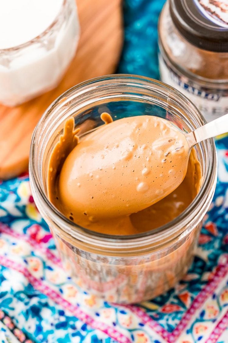 A spoon coming out of a mason jar with whipped coffee on it.