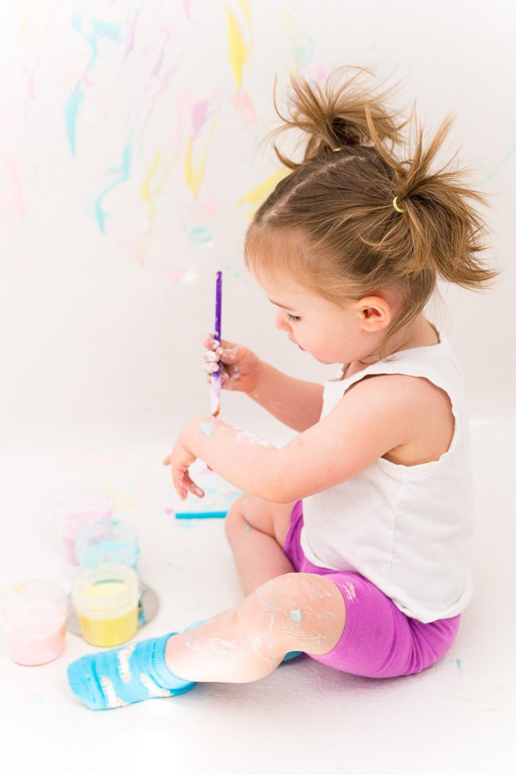 Toddler girl painting with bath paint.