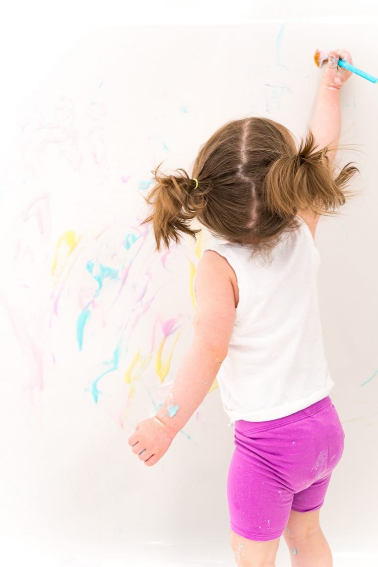 Toddler girl painting the tub with bath paint.