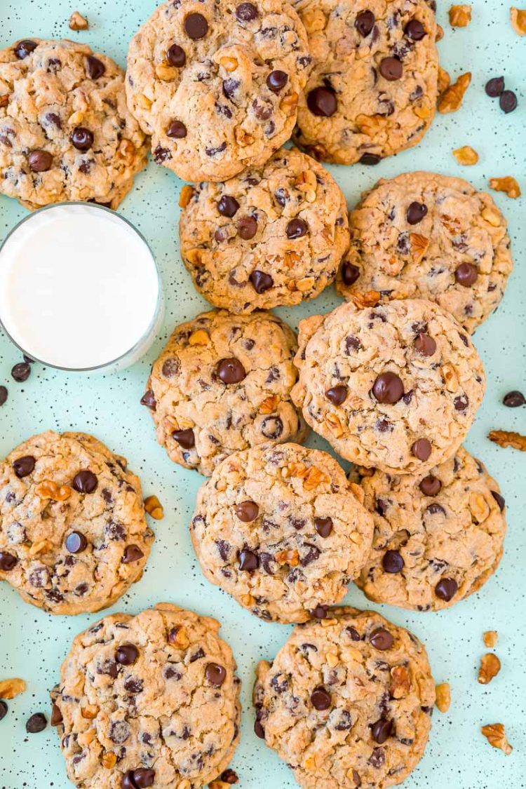 Chocolate chip walnut cookies on a baking sheet with a glass of milk.