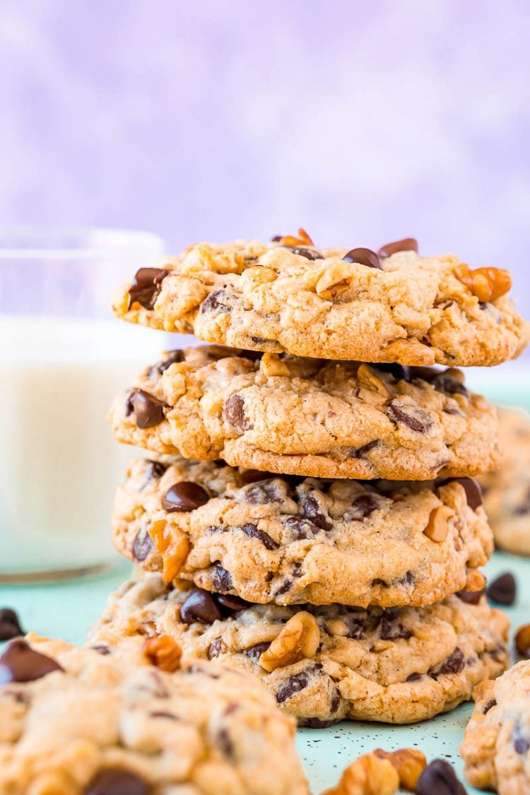 Four Doubletree cookies stacked on top of eachother with more cookies surrounding them and a glass of milk in the background.