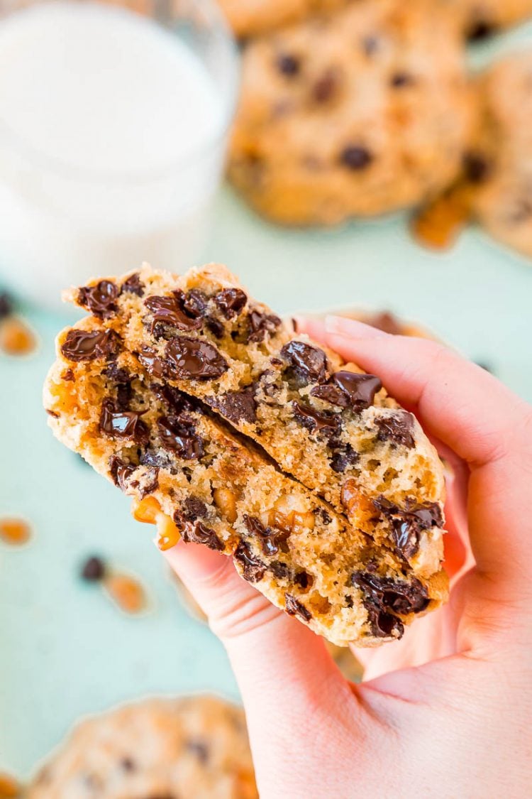 Chocolate chip cookie that has been broken in half being held by a woman's hand.