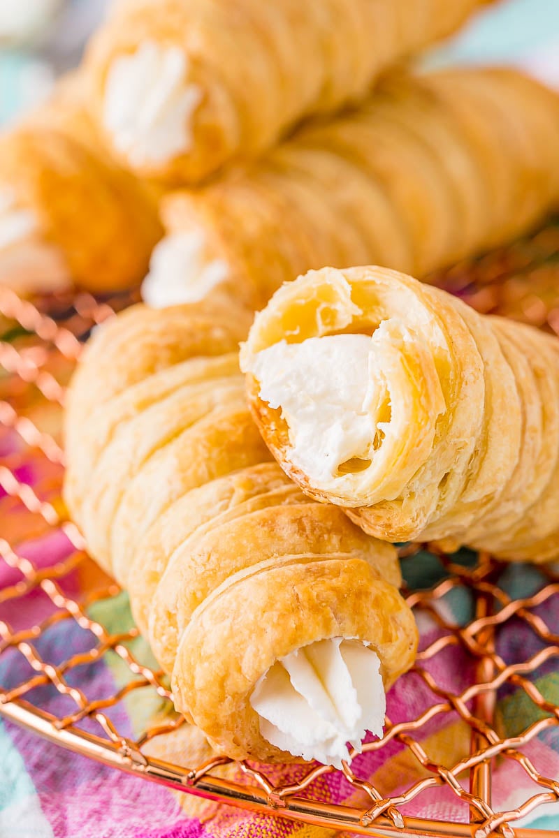 Cream horns on a wire rack, one has a bite taken out of it.