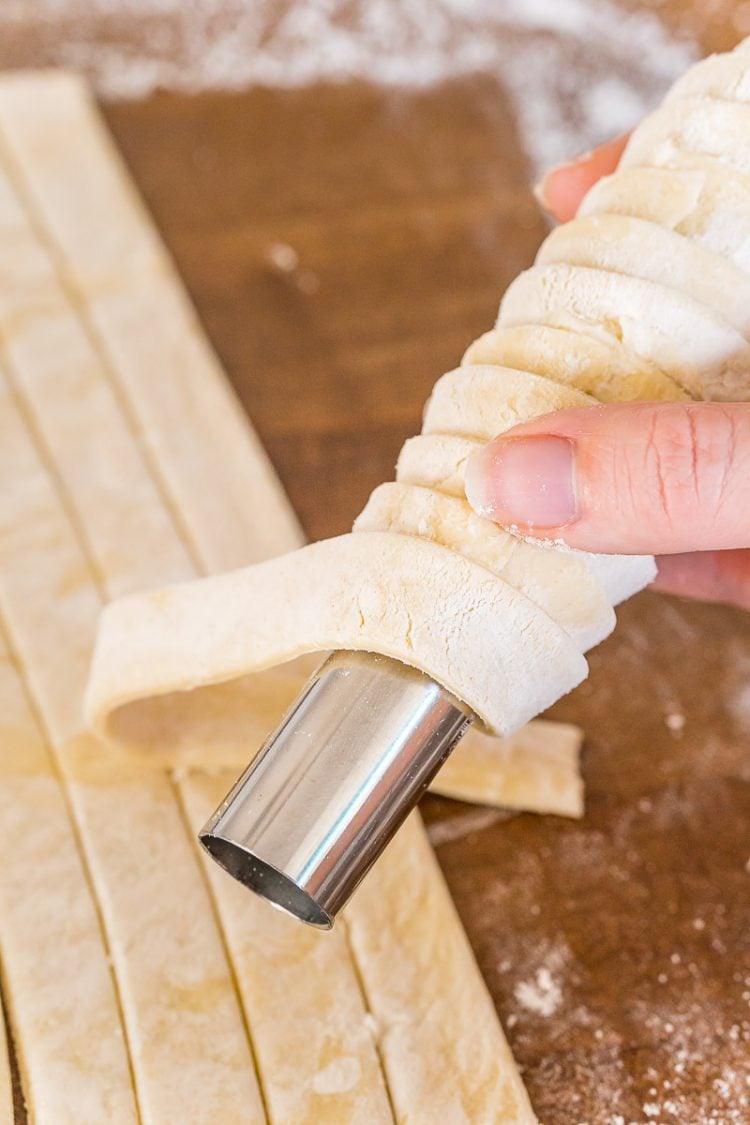Puff pastry dough strips being wrapped around a cream horn mold.