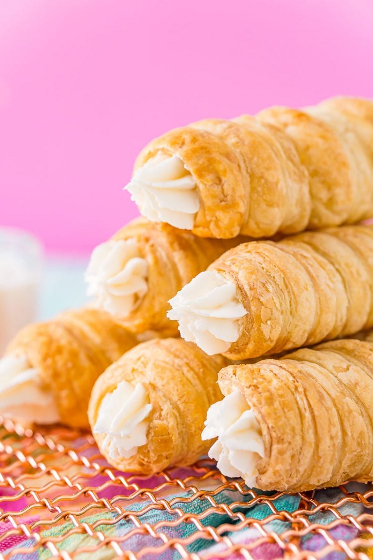 Six cream horns stacked on top of each other on a wire rack.