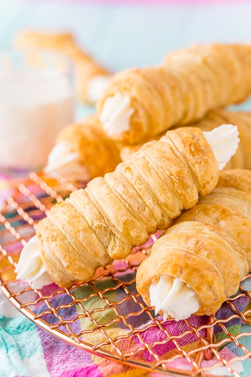 Cream horns stacked on top of each other on a wire rack with a glass of milk in the background.