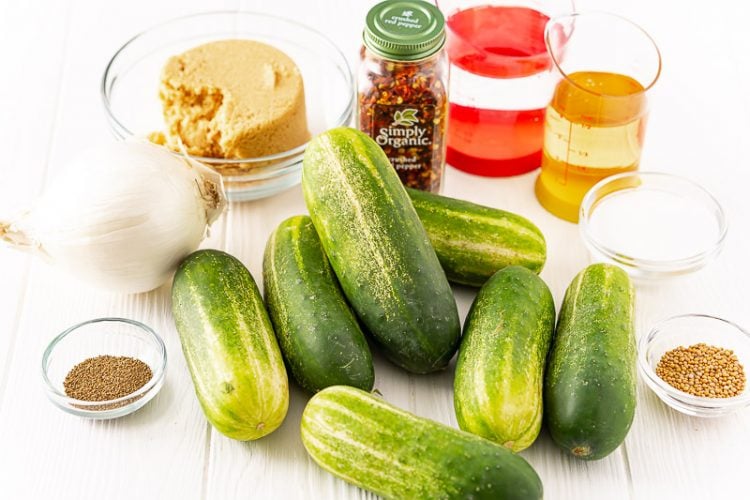 Ingredients to make bread and butter pickles on a white table.