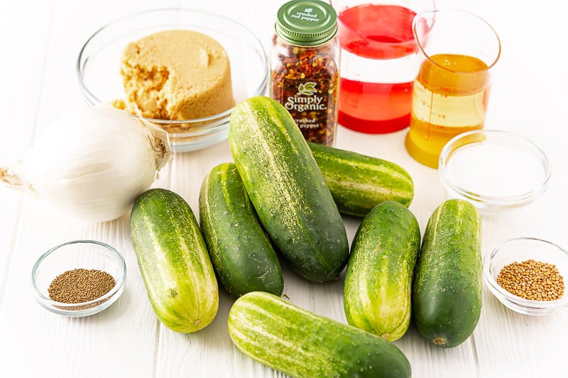 Ingredients to make bread and butter pickles on a white table.