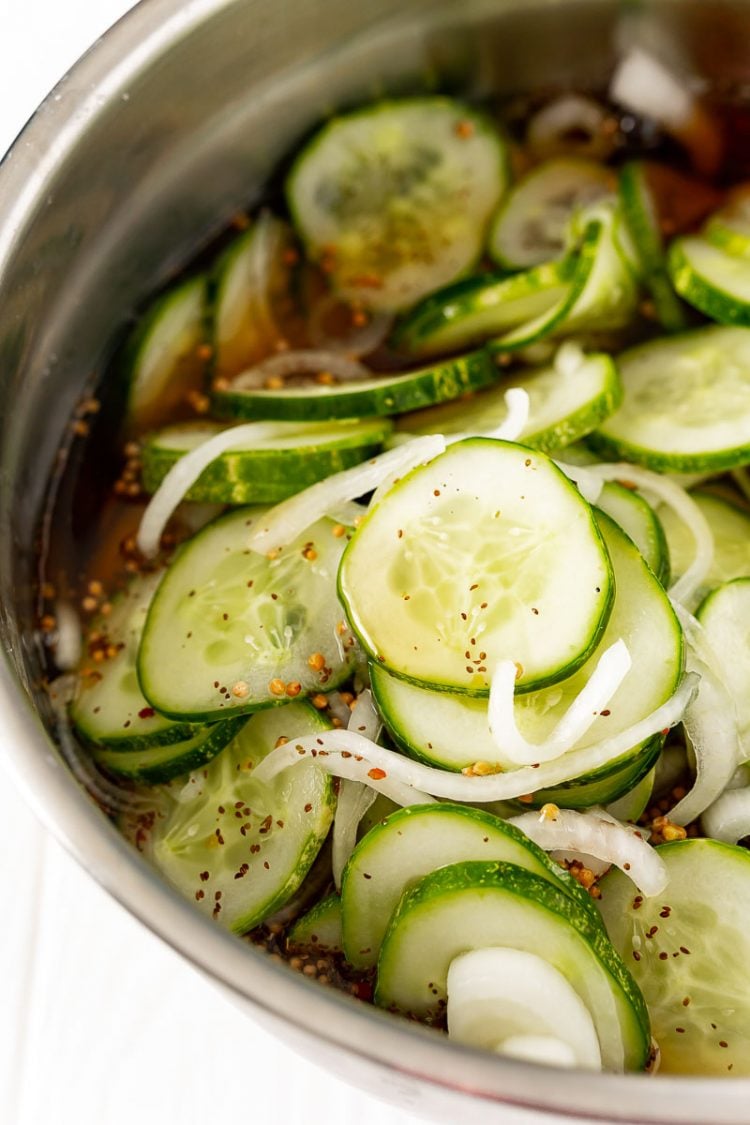 Sliced cucumbers and onions in a metal prep bowl with brine.