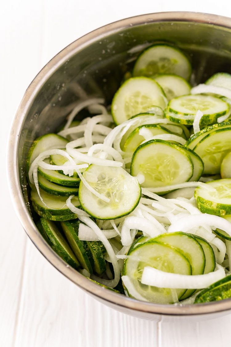 Cucumbers and onions slices and placed in a metal bowl.