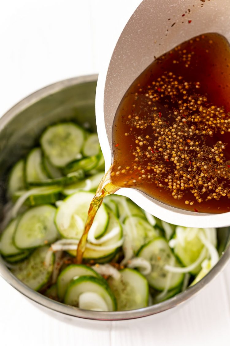 Brine being poured over sliced cucumbers and onions to make pickles.