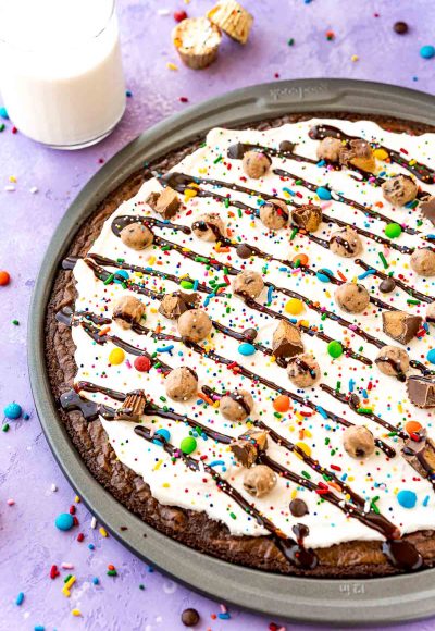 Close up photo of brownie dessert pizza in a pan on a purple surface with candy scattered around.